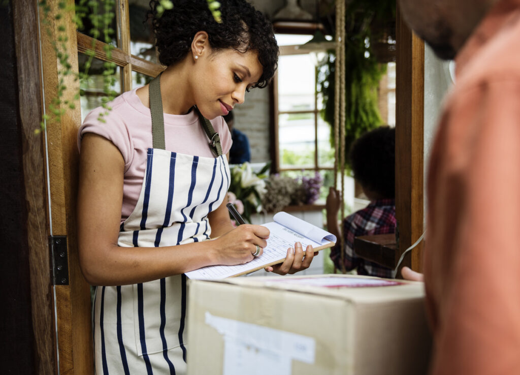 Mulher assina um clipboard para receber uma entrega de pacote em uma loja.