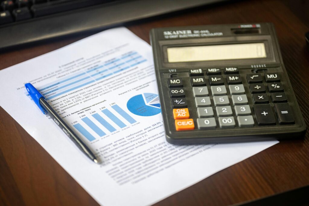 Calculadora sobre documentos financeiros com gráficos e uma caneta azul sobre mesa de madeira.