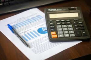 Calculadora sobre documentos financeiros com gráficos e uma caneta azul sobre mesa de madeira.